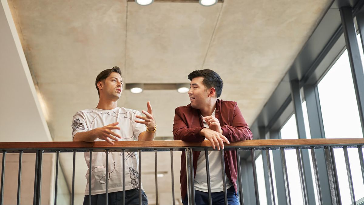 Two casually dressed men talking to each other while leaning on a railing