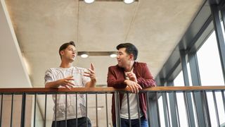 Two casually dressed men talking to each other while leaning on a railing