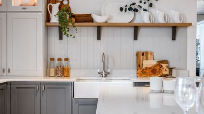 A white kitchen with grey cabinets, white counters, and a large white farmhouse sink