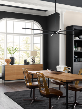 An open plan dining room with a dark accent wall, a wooden dining table, and a large window