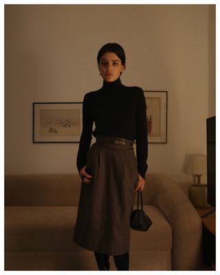 Woman wearing a turtleneck sweater, belt, and long skirt.