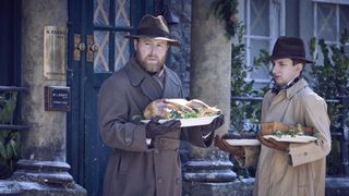 Samuel West and James Anthony-Rose in hats and coats as Siegfried and Carmody stand in the snow carrying food in All Creatures Great and Small.