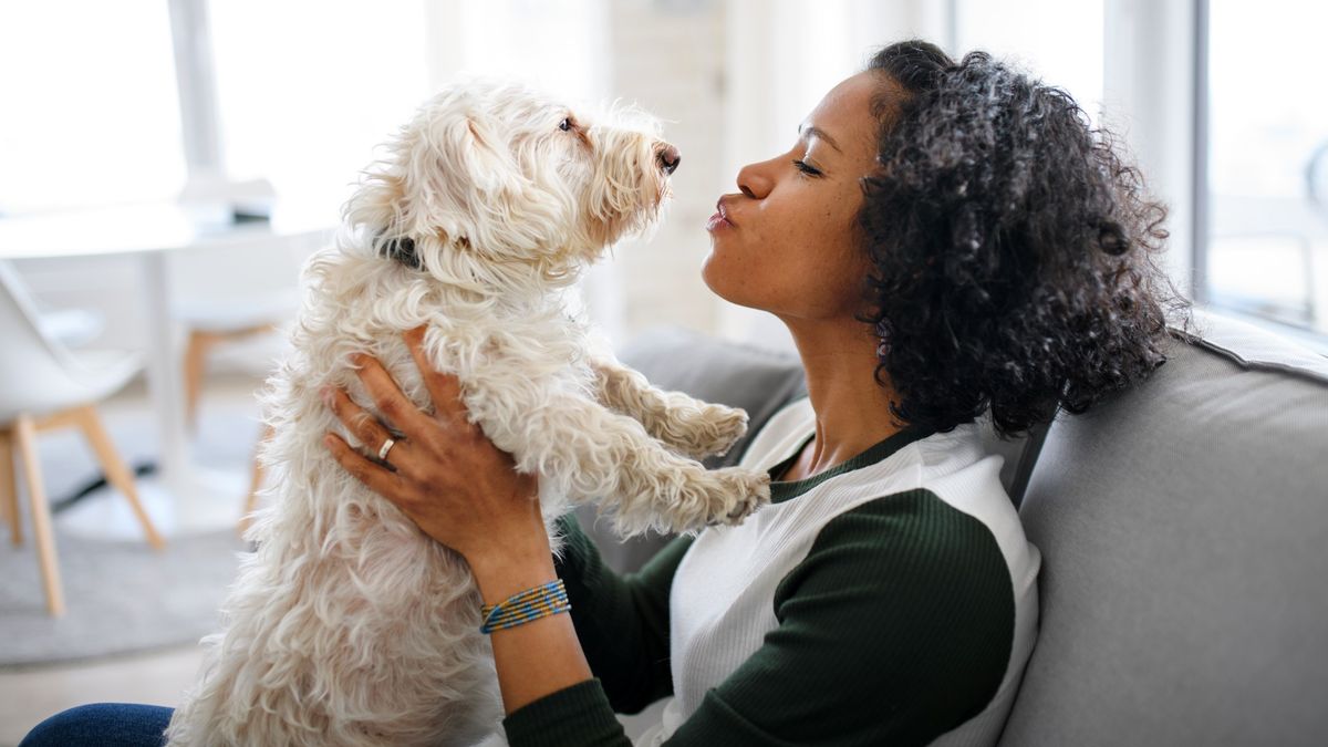 Woman sat on couch holding her dog up to her face