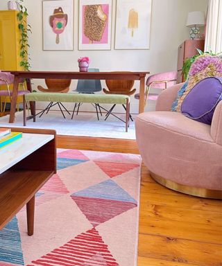 A small living room with a pink rug, pink chair, and brown coffee table and dining table