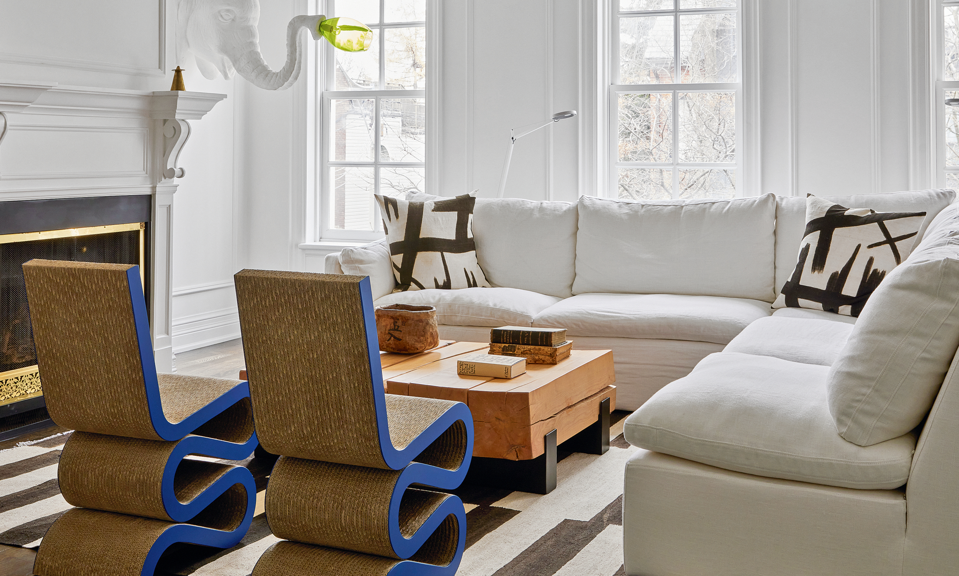White living room with corner sofa, abstract graphic black and white cushions, wood coffee table and cobalt blue Wiggle side chairs