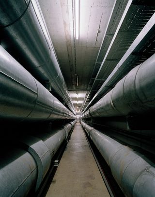 A long underground corridor with large pipes running along the walls.