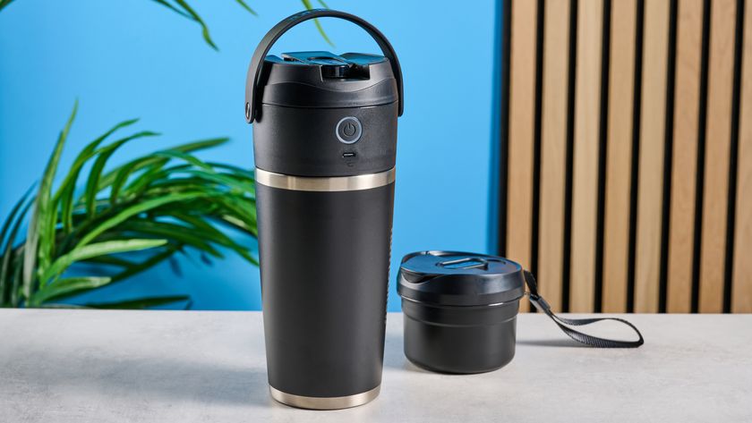 the Nutribullet Flip with a black insulated tumbler and a portable battery-powered blade photographed with a blue background. The tumbler has a carry strap and a sippy lid you can interchange, and an on/off button on the base. 