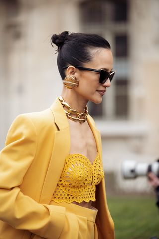 Anna Rosa Vitiello wears yellow blazer, pants, laced top, black bag, gold big chain necklace, golden shell earrings, and black sunglasses outside the Stella McCartney show during Paris Fashion Week - Womenswear Fall Winter 2023 2024 on March 06, 2023 in Paris, France