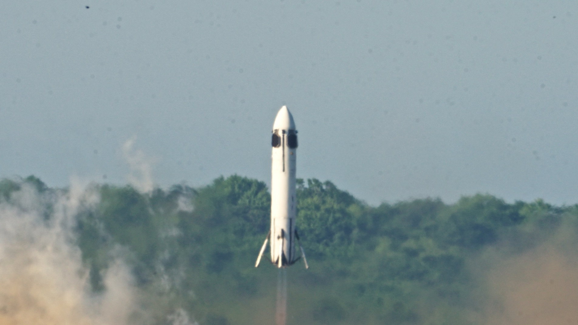 a small white rocket is seen just above the ground, with trees in the background