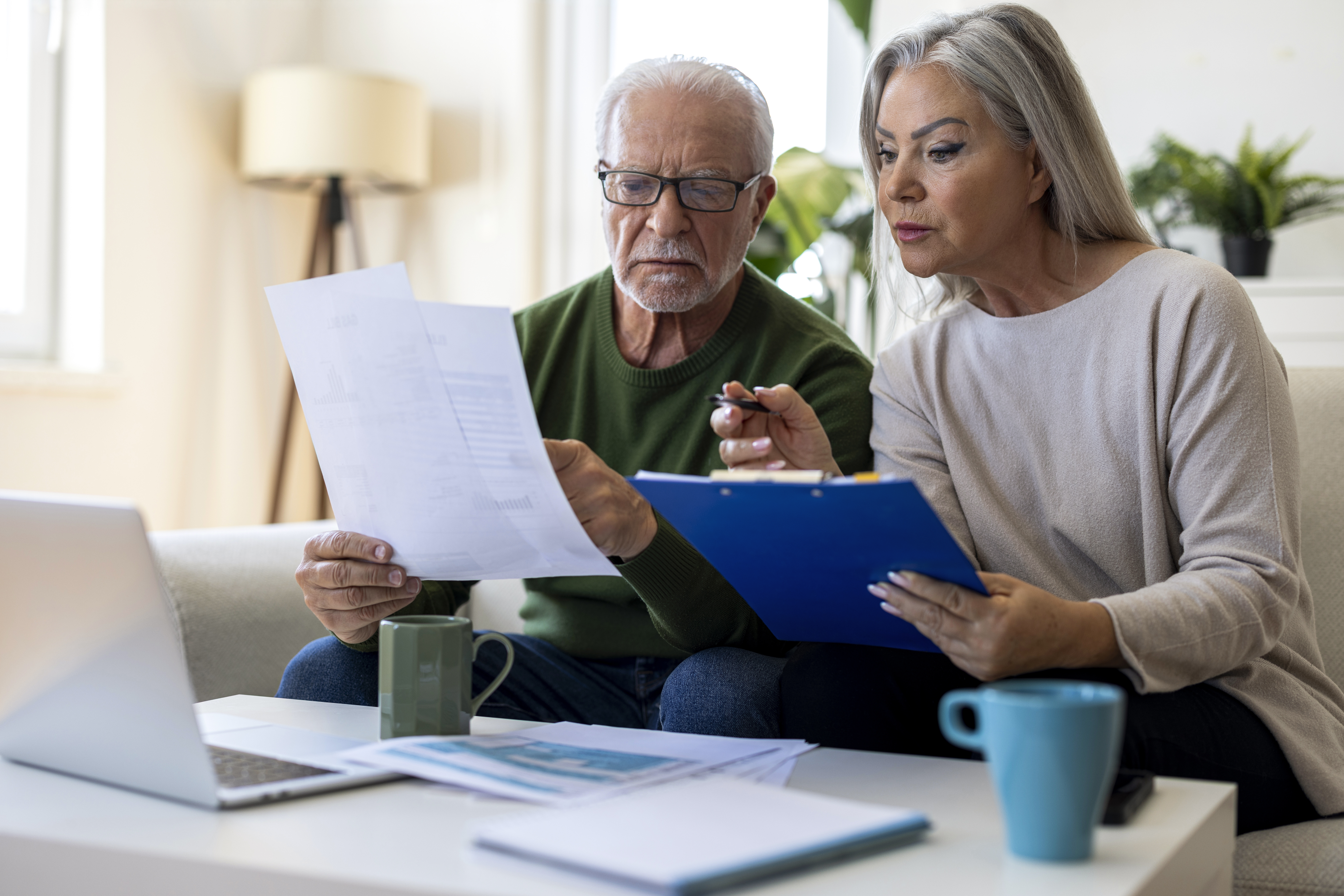 Senior couple sitting at home and reviewing bills, paperwork and financial documents