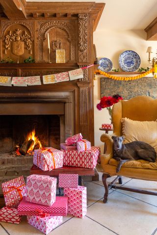 Christmas living room with handmade card garland, pink wrapped gifts, vintage mustard armchair, open fire lit