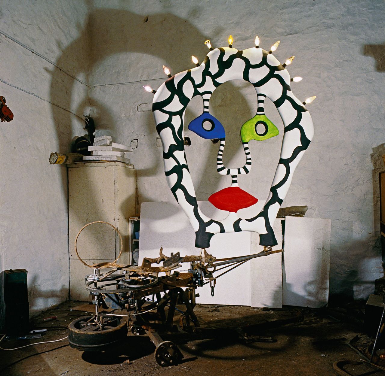 A colorful sculpture resembling the face of a woman with red lips, one green and one blue eye is lit up by lightbulbs and painted in a black and white motif.