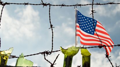 barbed wire fense with broken glass bottles and an american flag