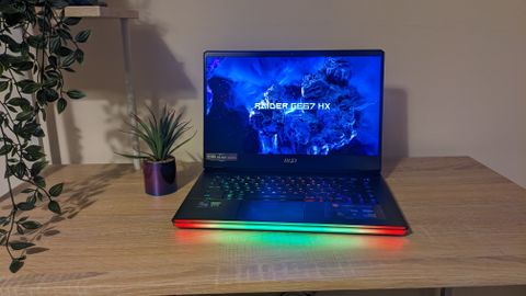 The MSI Raider GE67 HX photographed on a wooden desk with RGB lighting turned on.