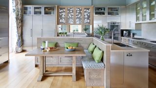 open plan kitchen diner with brushed chrome appliances and cabinets and a built in seating area with wooden table and green cushions
