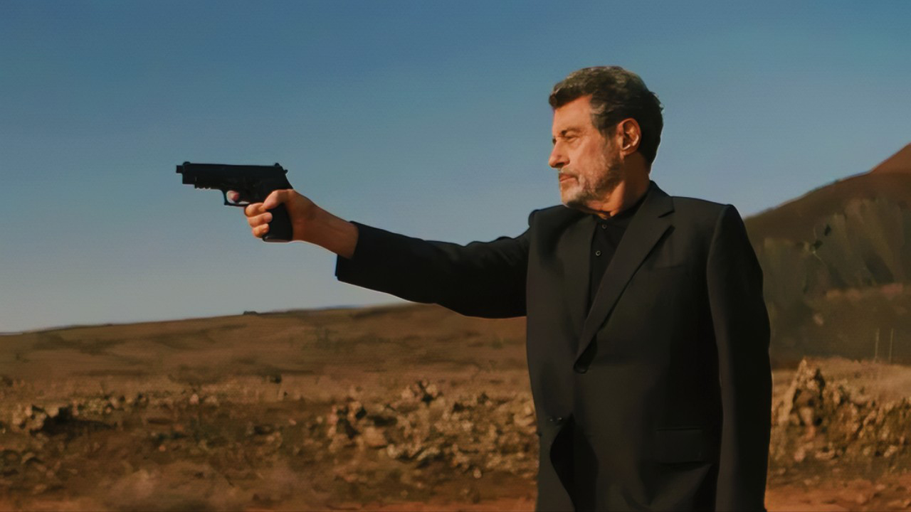 A still from the movie American Star showing Ian McShane's character Wilson in the desert holding a gun.