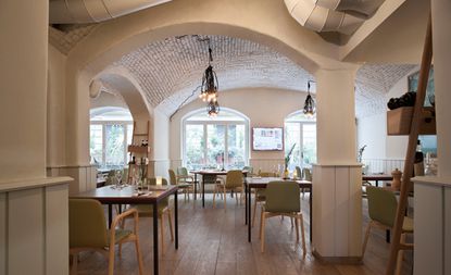 Restaurant with a neutral interior and huge windows that let in a lot of light, complete with brick ceilings in white.