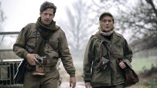 Andy Samberg and Kate Winslet as David Scherman and Lee Miller waling outside in Europe during World War II with cameras in Lee