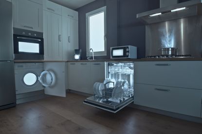 Lights from appliances, including a washing machine, dishwasher, microwave and oven in a dark kitchen.