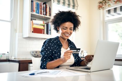 smiling woman on laptop with bank card in hand