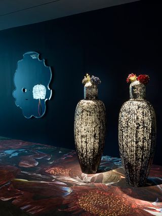Two large, tall sculptures with flowers on lid and mirror on the wall