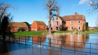 large brick house with outbuildings in rural setting with water breaching fence and heading towards property