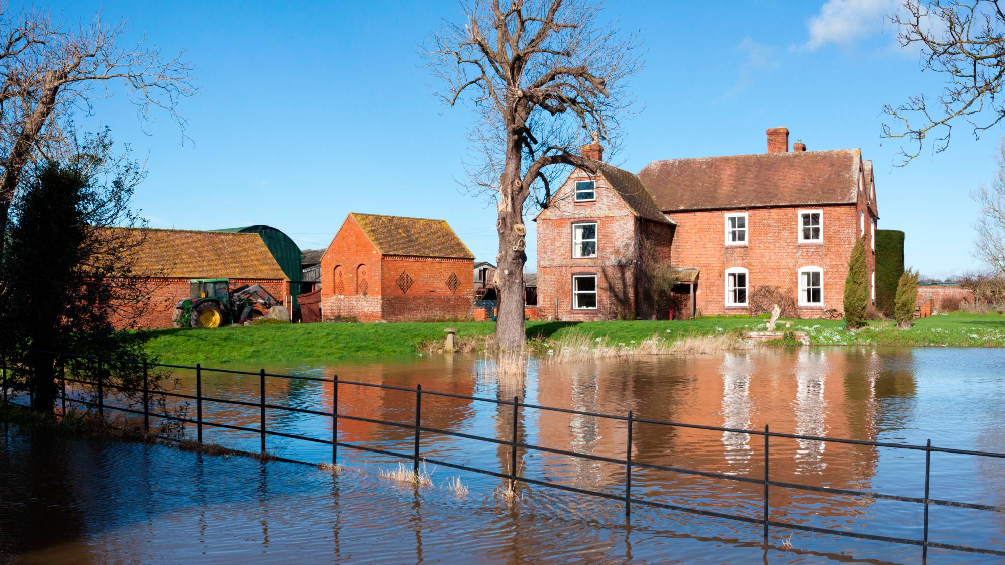 large brick house with outbuildings in rural setting with water breaching fence and heading towards property