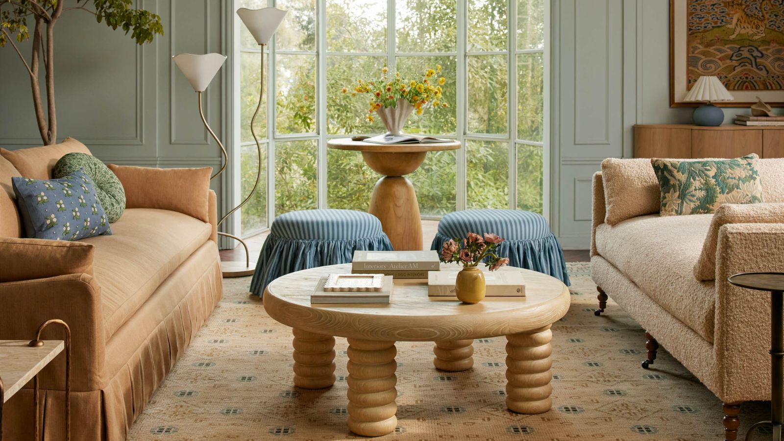 Blue living room with cream and beige sofas, patterned rug, round wooden dining table