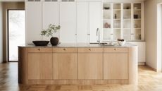 a contemporary minimalist kitchen with a large oak island with cabinets within and behind it, a row of white cabinetry, half with glass doors