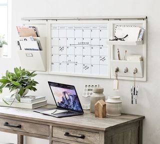 A home office with wooden desk and overhead organization system with wall calendar and stationery storage