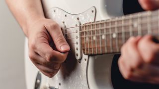 Man playing a white Stratocaster with a guitar pick