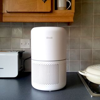 The Levoit Core 300S air purifier in a kitchen with a dark work surface and wooden kitchen cupboards