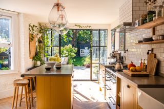 A bright kitchen with crittal doors open to a courtyard a yellow island in the middle of the room