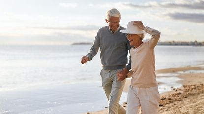 Two older adults smile and laugh as they walk together on the beach.