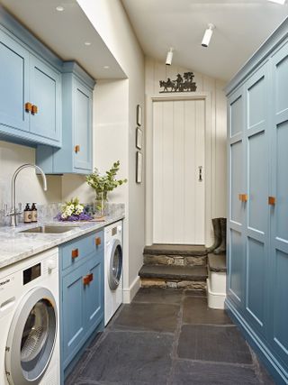 Blue cupboards with a dark grey stone floor, built in washing machine and a sink