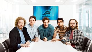 En promobild för HBO Max-serien Silicon Valley, där huvudpersonerna sitter runt ett kontorsbord och kollar mot kameran.