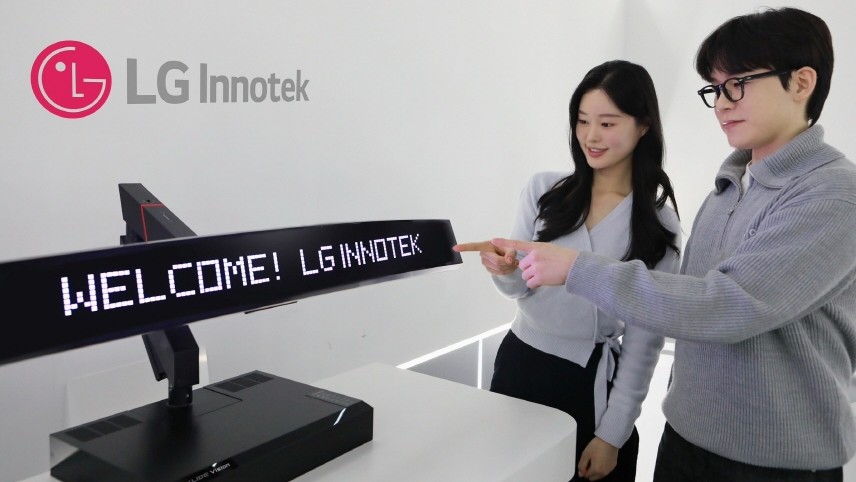 A man and a woman stand next to an LG Innotek display showing &quot;WELCOME! LG INNOTEK&quot; in bright white text.