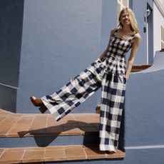 Model wearing a nobody's child blue and white gingham two piece trouser set in front of a blue building