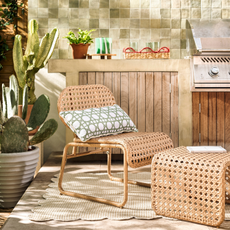 Habitat global accent chair and footstool on cream scalloped rug on patio. Behind is a silver bbq and wooden sidebaord. A cactus is the left of the chair.