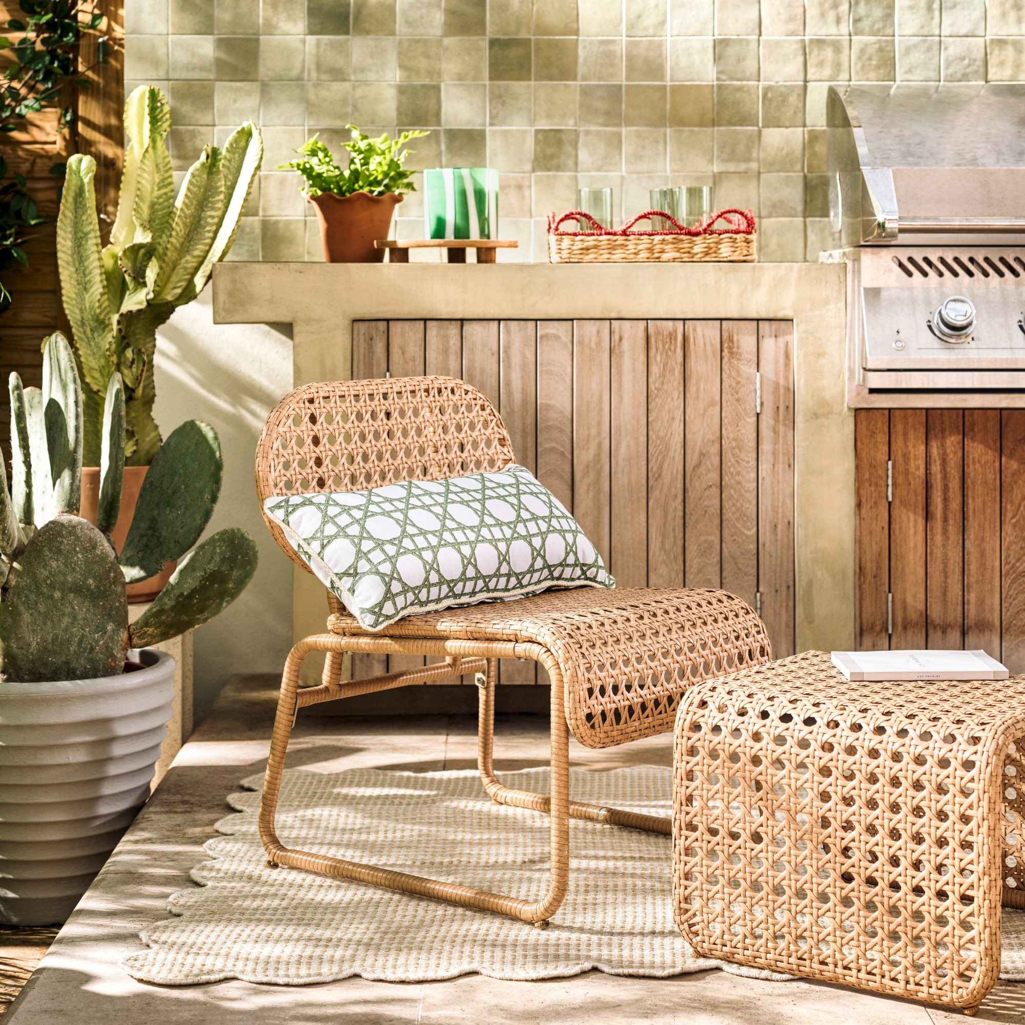 Habitat global accent chair and footstool on cream scalloped rug on patio. Behind is a silver bbq and wooden sidebaord. A cactus is the left of the chair.