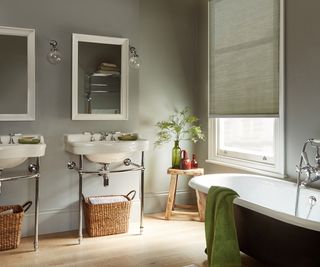 large bathroom with white bath, double sinks, green walls and green roller blind