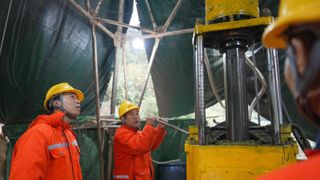 A group of miners stand around a drill wearing high viability gear