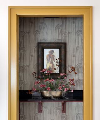 pantry with gray patterned wallpaper with artwork, ledge with display of pink flowers and yellow-gold painted doorway trim