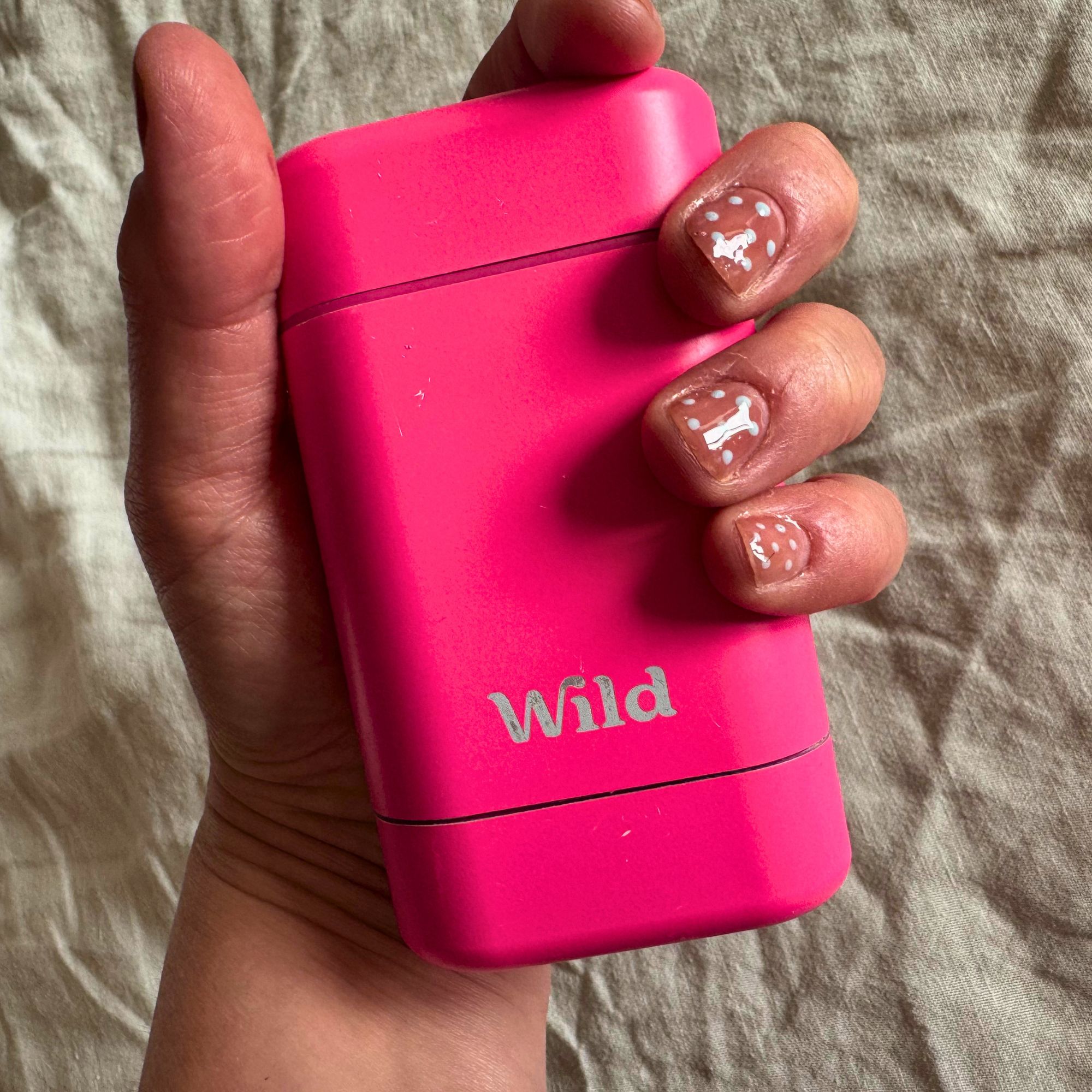 A real-life shot of writer Heidi Scrimgeour holding her Wild refillable deodorant case, with linen bedding visible in the background