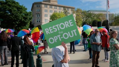A person holds a sign that reads 'restore the opt-out' 