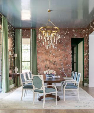 dining room with copper wallpaper, green curtains, gold chandelier, wooden dining table and blue and white dining chairs