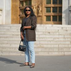 A woman wearing red lipstick, a blazer, and jeans, with goddess braids in her hair.