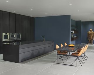 A black kitchen idea with black cabinets, blue walls, and orange dining chairs