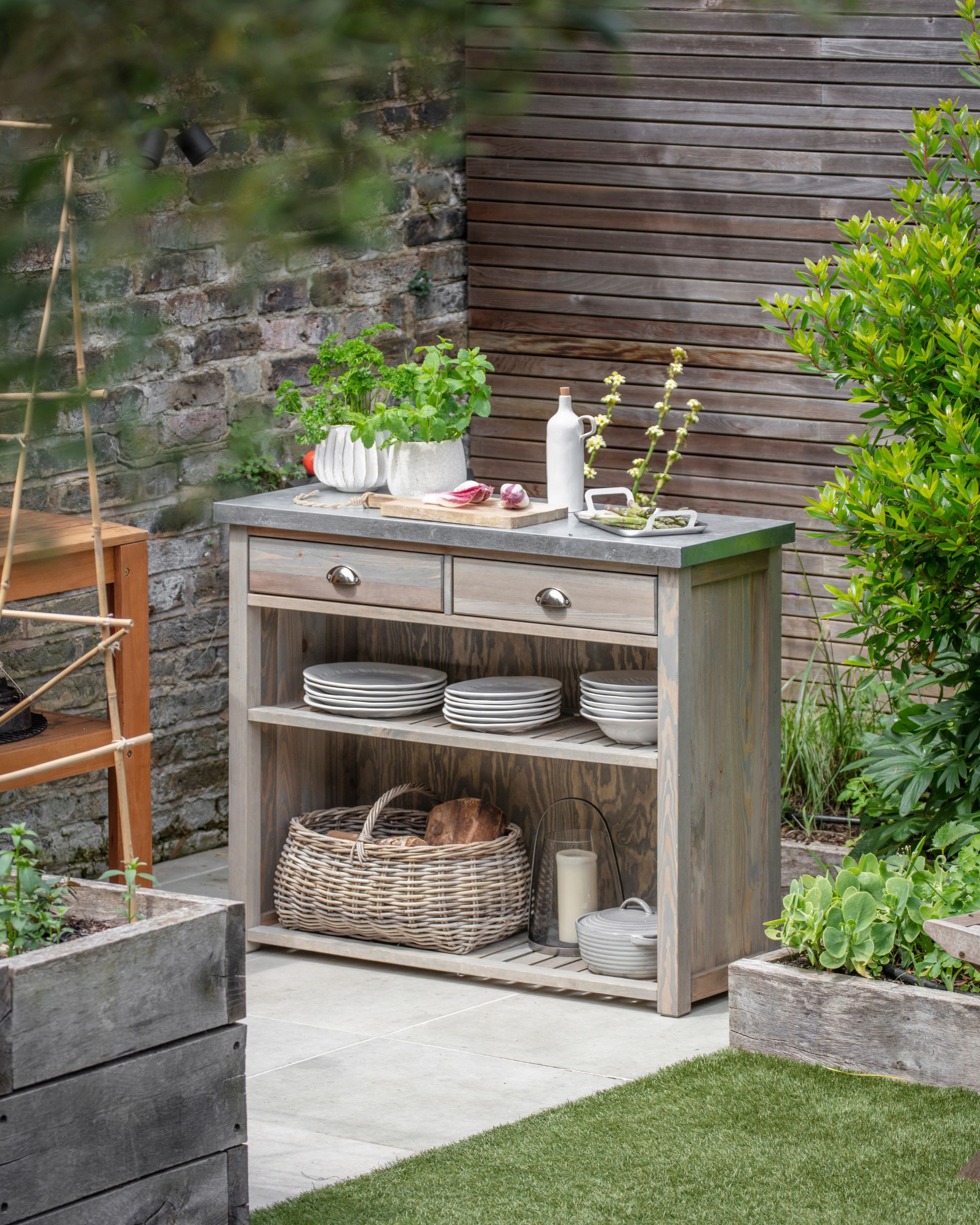 Outdoor storage unit with shelves and drawers, and a metal worktop in a modern garden.