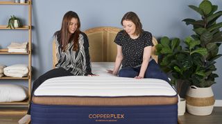 Two girls sitting on Brooklyn Bedding CopperFlex mattress in sleep studio with shelf and plants